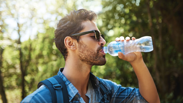 Man with sunglasses drinking a bottle of water in a forest